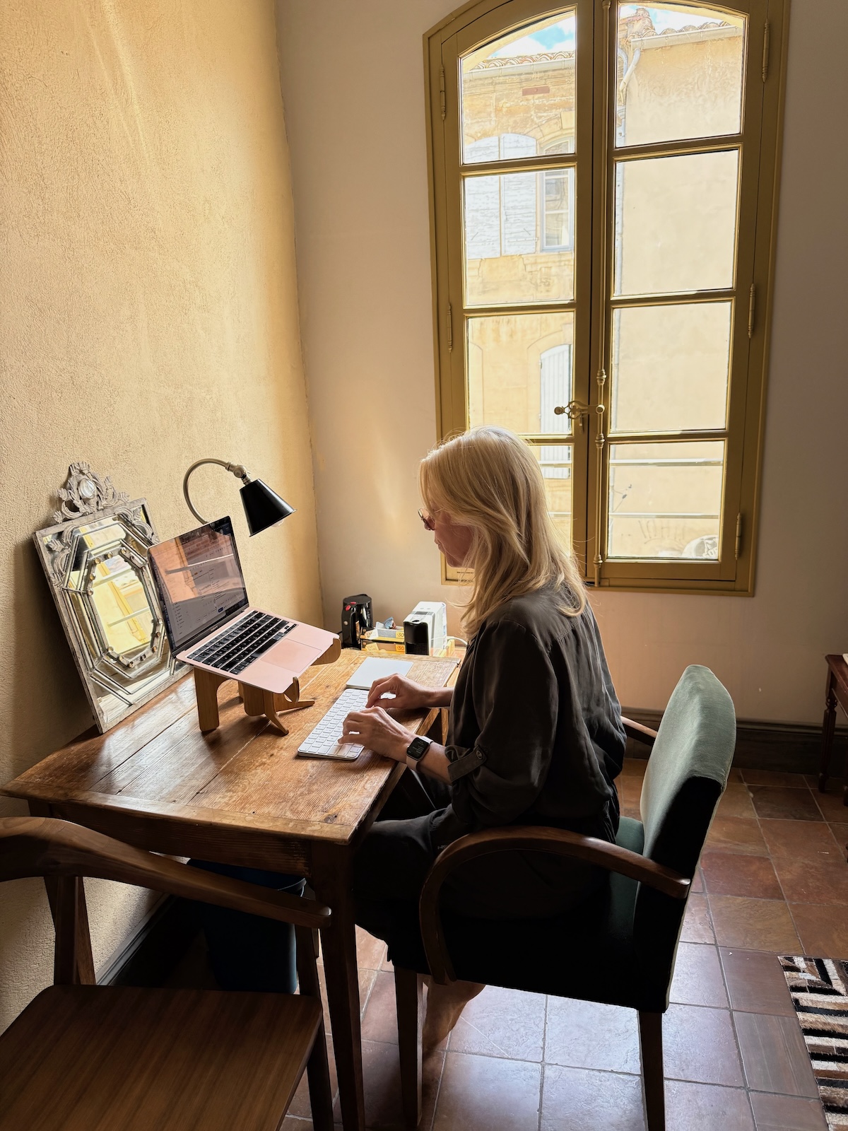 A Furies writer at a wooden desk by an arched window in the Arles house, afternoon light