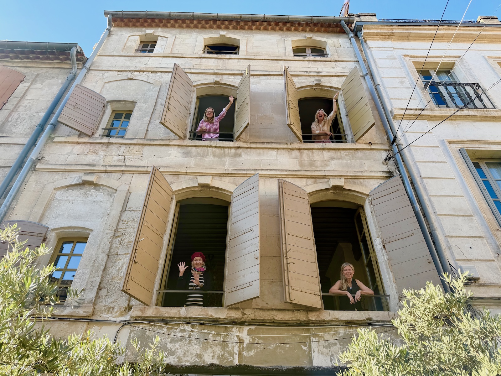 Four Furies writers leaning from the arched windows of the Arles stone house, waving and laughing