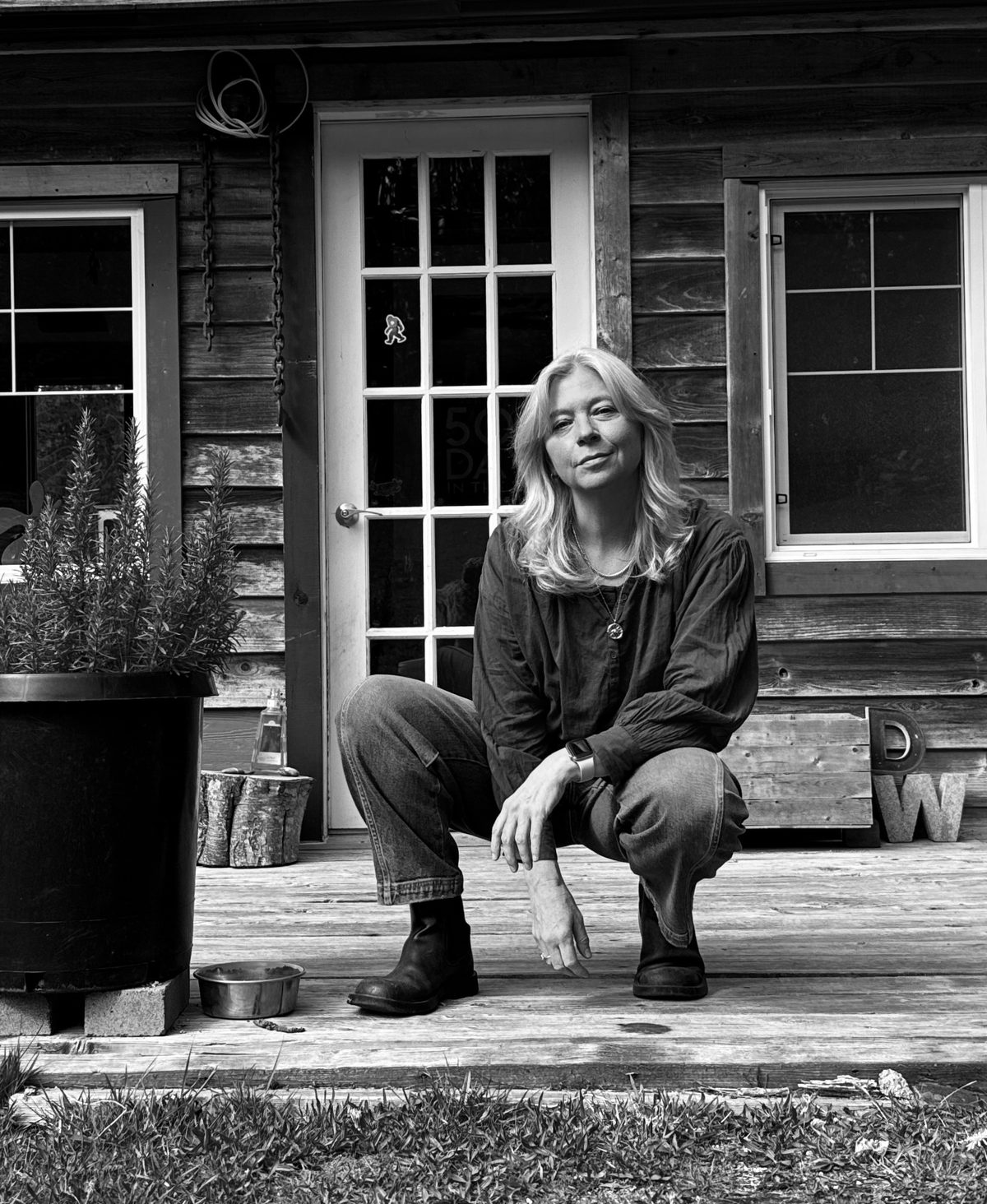 Maggie Langrick crouched on a wooden cabin porch, a concrete letter W beside her